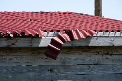 Part of a red metal roof coming off with dents in it from a storm.