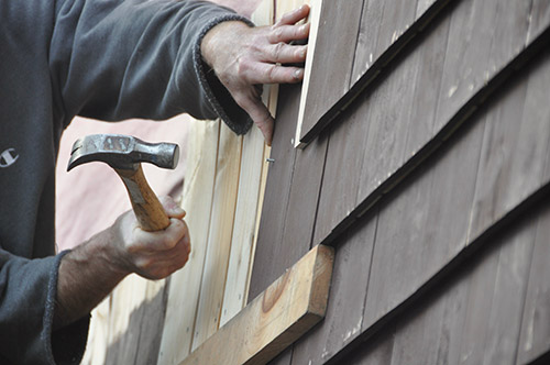 A person is installing wood shingles on a building.